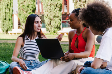 Multicultural students collaborating on a laptop in university campus park