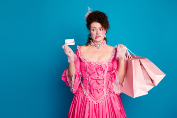 Young woman in pink corset dress holds shopping bags and card with playful expression, against a...