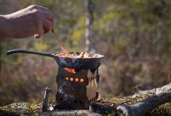 Male hand stirring in a frying pan over a hobo stove in the forest