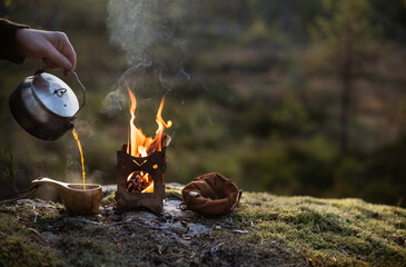 Coffee brewed on a firebox is poured into a wooden cup in a forest landscape