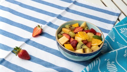 A bowl of colorful tropical fruit set against a vibrant blue striped tablecloth, casual, exotic fruit, lively, bright, blue striped background