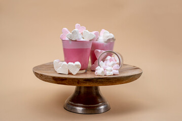 Marshmallows in Herzform in rosa und weiß, Platziert auf einem rosafarbenem Getränk mit Sahne und Zuckerstreuseln.