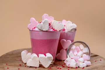 Marshmallows in Herzform in rosa und weiß, Platziert auf einem rosafarbenem Getränk mit Sahne und Zuckerstreuseln.