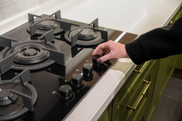 Woman arm turns on black gas stove in the kitchen close up