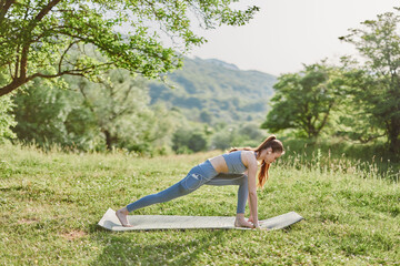Young woman practicing yoga outdoors on a mat in a serene green landscape, enhancing fitness, mindfulness, and healthy lifestyle