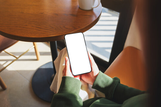 Mockup image of a woman holding mobile phone with blank desktop screen in cafe