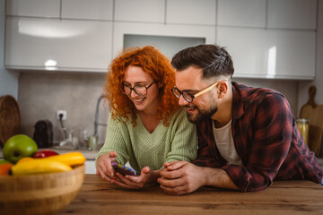 beautiful young happy couple stand and use mobile together at kitchen