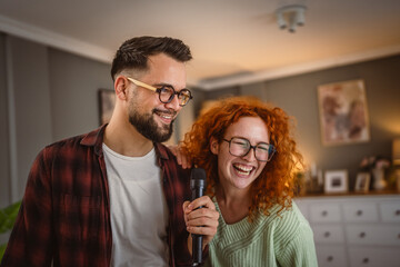 cheerful couple have a home party sing on microphone and dance at home