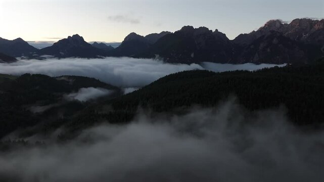 A mist-filled valley in the Dolomites at sunrise, with sunlight highlighting the peaks and dense alpine forest below. Taken near Danta village. Aerial photo with Dolomites. Hike in Italy. 4k video