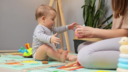 A young child is engaged in play, exploring various colorful toys and building blocks on a soft mat. An adult is nearby, nurturing the child's curiosity and creativity