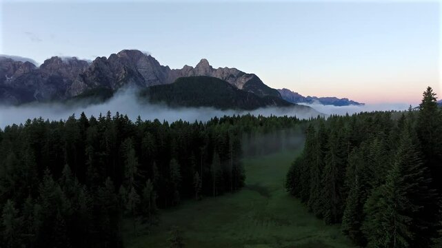 Sunrise over the Dolomites with vibrant hues on the Antelao and Cridola peaks, framed by dense alpine forests below. Captured near Danta village, Italy. Hiking in Italy. Aerial 4k video.