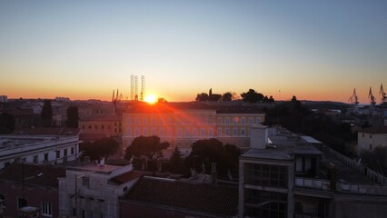 Fototapeta premium A stunning aerial view of Pula during sunset, capturing the warm, golden hues of the sky as they blend with the vibrant blue of the Adriatic Sea. This beautiful landscape offers.