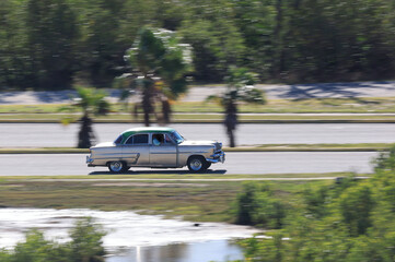 A vintage car drives along a country road on the Caribbean island of Cuba, Caribbean, Central America..