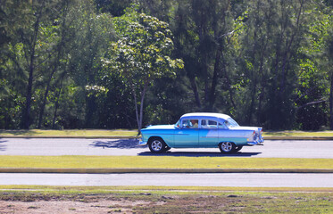 A vintage car drives along a country road on the Caribbean island of Cuba, Caribbean, Central America..