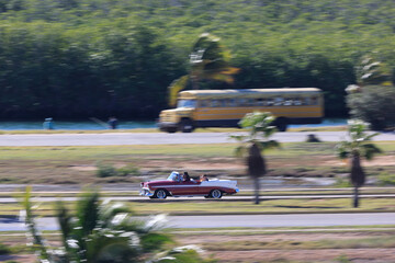 A vintage car drives along a country road on the Caribbean island of Cuba, Caribbean, Central America..