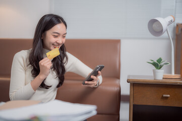 Happy freelancer holding a credit card while using a smartphone for online shopping at home,...