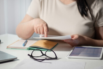 Female paying bills at home. Woman holding invoice in hands and calculates amount of debt. Bill payment online concept.