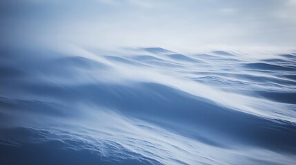 Windswept snowdrifts creating abstract wave patterns on a snowy landscape under a cloudy sky.