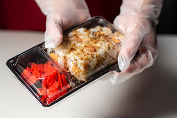 Sushi to go concept. Take away box with sushi rolls in woman hands in gloves. Food delivery concept. Take away food concept.