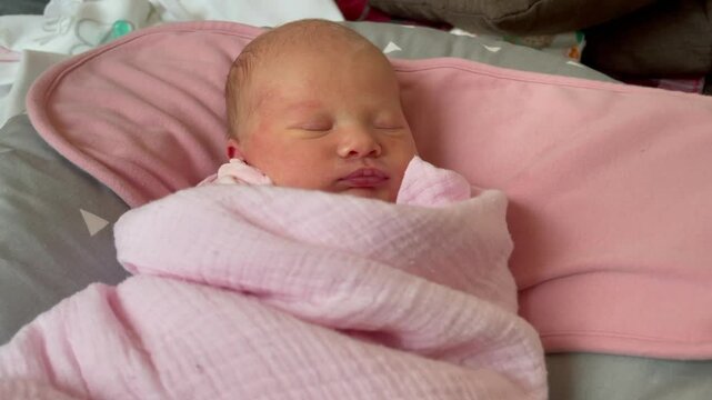 Close-up of a newborn baby lying in the lounger swaddled. The baby is two weeks old and shows typical features of a newborn baby: flaking skin and pimples, slight redness of the face. 
