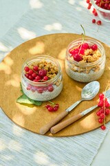 Breakfast or dessert, chia pudding with granola and fresh redcurrant berries in glass jars on light concrete background. Chia seed pudding recipes. Healthy food.