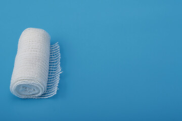 Close-up of a roll of sterile white gauze placed on a clean blue background. Perfect for illustrating medical, healthcare, and first aid concepts