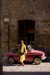 Stylish woman standing next to a classic convertible on a rustic street. A perfect combination of...