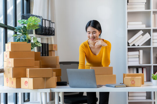 Online Business Success: A confident and joyful entrepreneur manages her thriving online business, surrounded by a stack of shipping boxes.