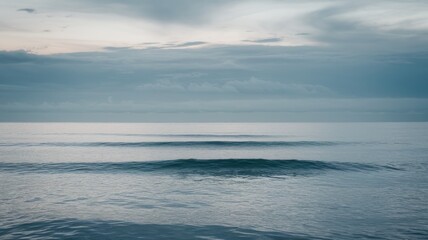 Obraz premium A tranquil seascape featuring gentle waves under a serene, overcast sky. The soft colors create a peaceful and calming atmosphere.