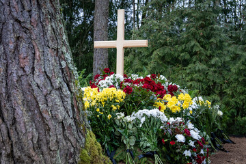 Freshly Decorated Grave with Wooden Cross and Colorful Flowers - Peaceful Cemetery Scene. Funeral Arrangement with Wooden Cross and Floral Wreaths in a Forest Setting.