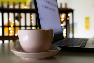 Close-up of a hot coffee cup and laptop on an office desk in a cozy cafe. Ideal for business work, remote work, and freelance lifestyle concepts in a comfortable setting.