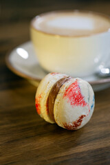 Colorful macaron beside a warm cup of coffee on a wooden table during a relaxed afternoon
