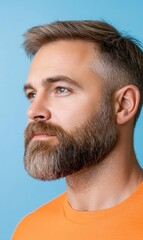Obraz premium Thoughtful man with beard in orange shirt posing against blue background capturing modern masculinity and style