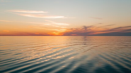 Fototapeta premium A serene sunset over calm ocean waters, with gentle waves reflecting a palette of orange and blue hues.
