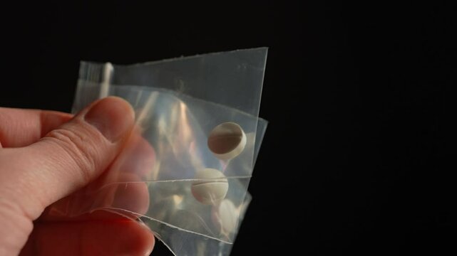 Hand of the drug dealer show off and lure with prescription opioid pill in small plastic bag for sale in clubs, parties and street to addicts. Illegal drugs trafficking, cause dependence and overdose
