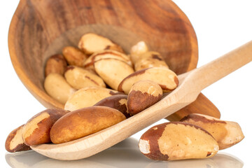 Brazil nuts without shells with wooden cup and spoon, macro, isolated on white background.