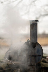 Smoke comes from black offset smoker grill in home backyard, family patio, barbeque party on open...