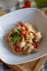 plate of homemade gnocchi with tomato and basil in a white bowl with a checkered tablecloth