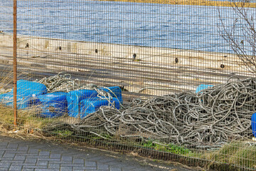 Pile of Crab Pots and Lobster Pots Made from 20L Blue Plastic Jerry Cans and Nautical Rope Piled Up on Harbour Quayside Behind Chain-Link Fence Stored for Winter