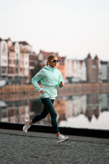 Motion photo of a young pretty woman in a mint jacket jogging along the embankment in the city