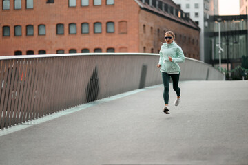 Young sporty woman in a jacket and glasses is running on the pavement