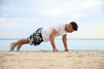 Muscular man doing push up on beach. Body training