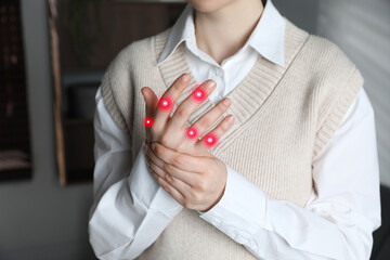 Woman with joint inflammation indoors, closeup. Red areas on fingers