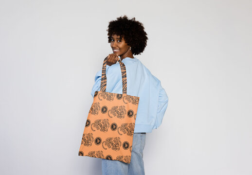 Black woman with afro hair  smiles while holding a blank tote bag, perfect for customizing with your logo or design.