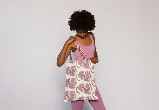 Mockup of black afro woman in activewear holds a blank tote bag 