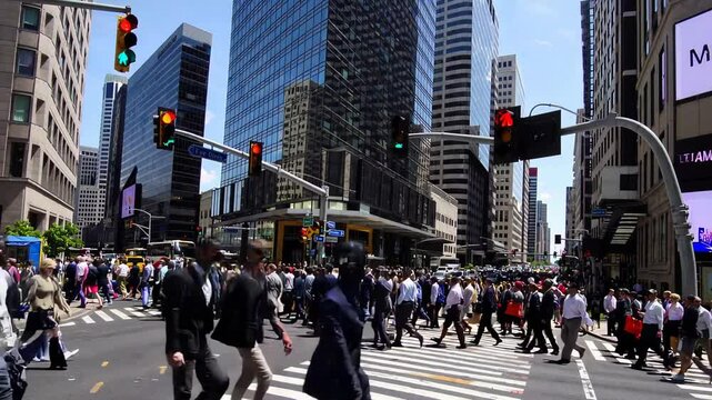 bustling city intersection with a large crowd crossing the street among towering skyscrapers, traffic lights, and urban energy under a clear blue sky.