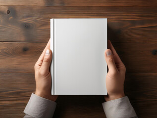 Obraz premium a hand holding a blank hardback book on a wooden desk, ideal for showcasing custom book cover designs.