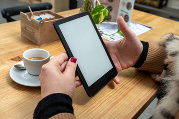 Close-up of hands holding an e-reader with coffee on a wooden table