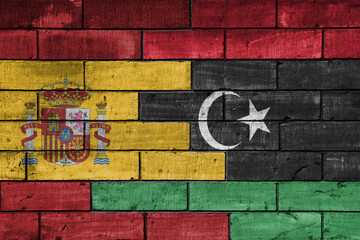 colourful painted big flag of spain and flag of libya on a massive old brick wall background. concept