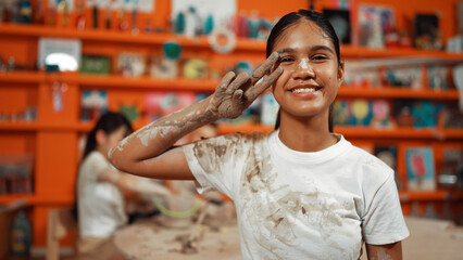 Happy caucasian girl pose at camera while diverse children modeling clay behind. Cute student...